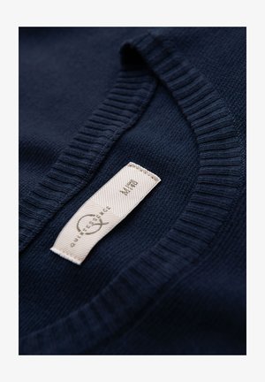 Navy blue knitted sweater with a ribbed neckline. Label visible with text "QUINTESSENCE" and size M. Soft texture, close-up view.