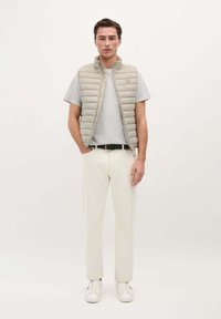 Lette beige puffer vest over en grå t-shirt, creme bukser og hvide sneakers. Vestene har en standkrave og lynlås lukning.