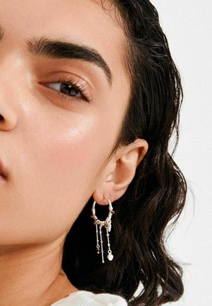 Orecchino a cerchio argentato con catene pendenti e piccole perle, caratterizzato da una superficie testurizzata e dettagli in oro a contrasto.