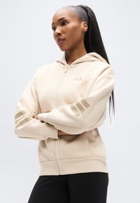 Μπεζ φούτερ με φερμουάρ κατασκευασμένο από μαλακό ύφασμα. Διαθέτει κουκούλα, μπροστινό φερμουάρ και τρεις ρίγες ως διακοσμητικό στα μανίκια. Λείο υφή και άνετη εφαρμογή.