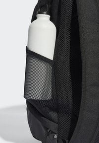 Schwarzer Rucksack mit einer Netz-Seitentasche, die eine weiße Wasserflasche hält. Strukturiertes Material, verstellbare Träger und sichtbare Reißverschlüsse.