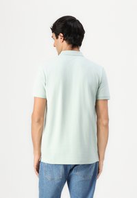 Lysegrønn polo-skjorte med korte ermer og krage, laget av et glatt stoff. Båret med blå denim jeans som har et enkelt design.