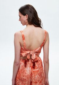 Oranje gebloemde crop top met een geknoopte achterkant. De stof lijkt lichtgewicht met dunne bandjes en een lichte textuur. Geschikt voor warm weer.