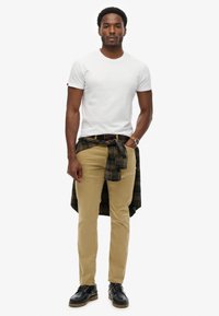 Biała dopasowana koszulka, khaki spodnie i czarne sznurowane buty. Ciemnozielona i żółta koszula w kratę związana w pasie, zegarek na lewym nadgarstku.