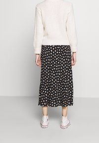 Knit cream sweater, black skirt with beige and white spots, paired with white canvas shoes. The outfit features a relaxed fit and layered textures.