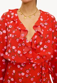 Vestido rojo con flores rosas, volantes en el escote y cintura atada. Collar de charm dorado con acentos de corazón y estrella.