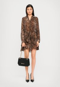 Woman wearing a brown and black leopard print dress, holding a black quilted handbag with gold chain straps, and black high heels.