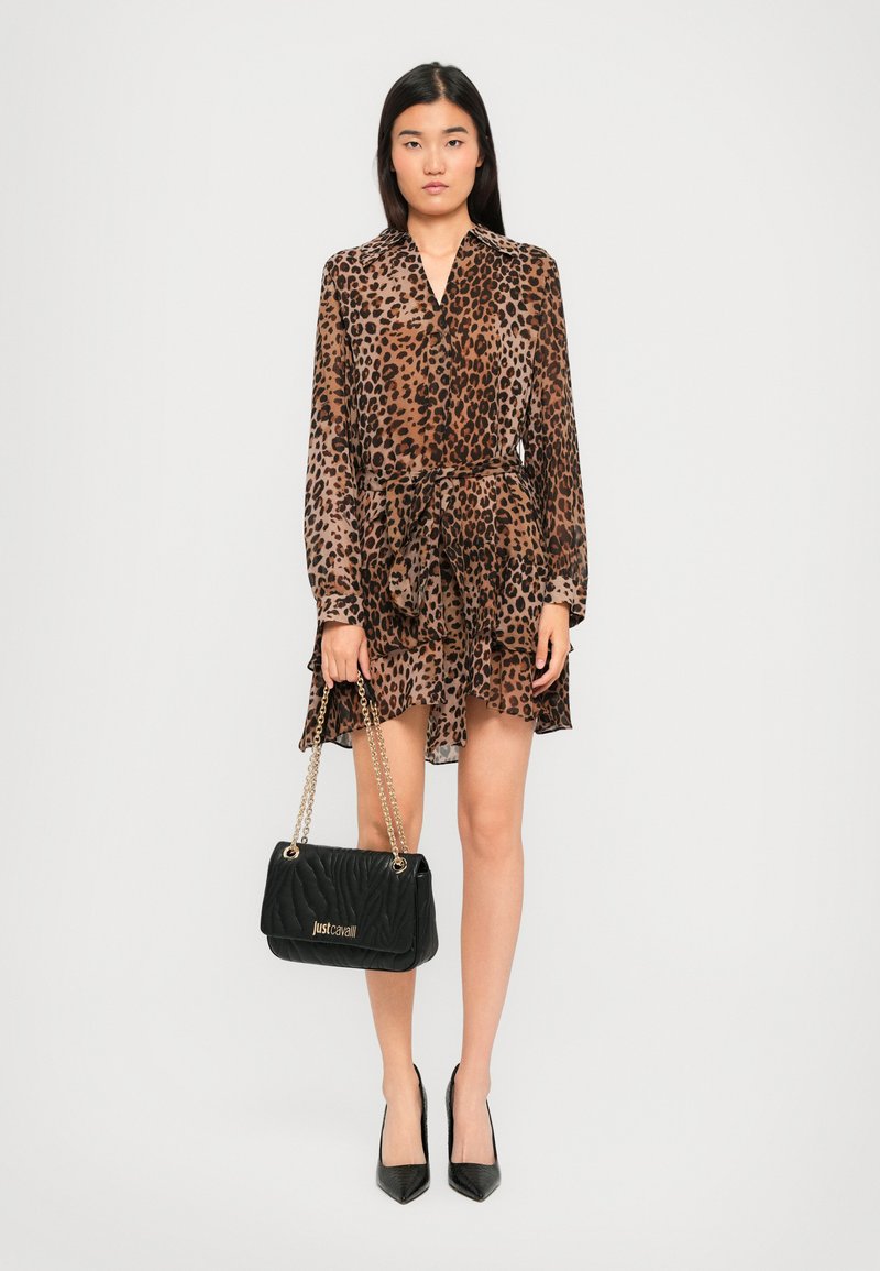 Woman wearing a brown and black leopard print dress, holding a black quilted handbag with gold chain straps, and black high heels.