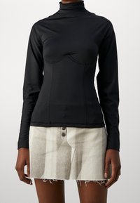 Svart långärmad topp med hög halsringning, figurnära design och sömdetaljer, bärs tillsammans med en texturerad grå minikjol.