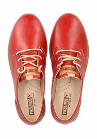 Scarpe di pelle rossa con punte rotonde, lacci beige e una soletta marrone chiaro con il marchio "Pikolinos" stampato. Texture liscia con accenti minimi.