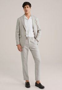 Helles graues kariertes Anzug mit taillierter Passform, einreihiger Blazer und Hose mit flachem Bund, kombiniert mit einem weißen Hemd und schwarzen Slippern.
