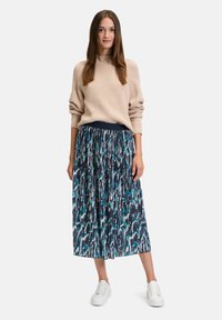 Beige gerippter Pullover und Midikleid mit navy Hintergrund und abstrakten Mustern in Türkis, Weiß und Pink. Weiße Sneaker.