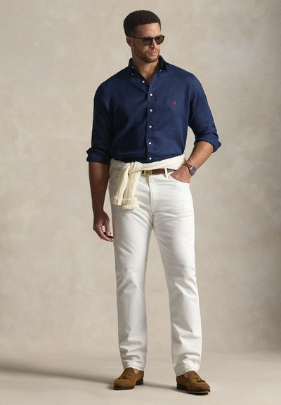 Navy zilas pogas krekls, baltas bikses, brūnas loafers kurpes. Džemperis sasiets ap vidukli, saulesbrilles, pulkstenis uz kreisās rokas. Vienkāršs dizains un viegls audums.