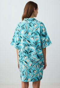 Abito floreale corto in azzurro chiaro, con bold pattern vegetali verdi e bianchi, vestibilità ampia, maniche larghe e dettaglio colletto.