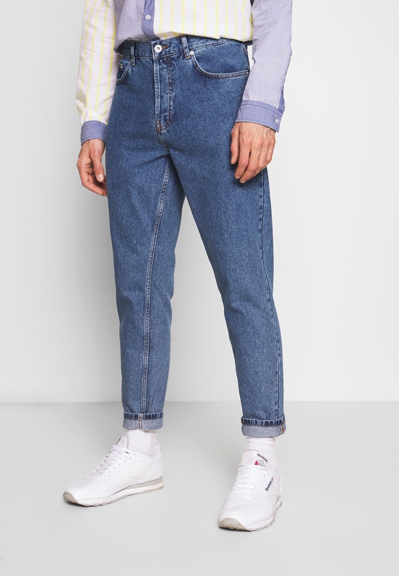 Vaqueros de mezclilla azul claro con un corte regular, piernas rectas, puños con dobladillo y diseño estándar de cinco bolsillos, llevados con zapatillas blancas.