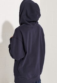 Námořnicky modrá oversized mikina s kapucí na stahování, měkkou strukturou, dlouhými rukávy a žebrovaným lemem. Vyrobena z bavlněné směsi.