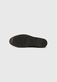 Black shoe sole featuring textured rubber, a smooth edge, and contrast stitching along the side. Logo visible on the midsole.