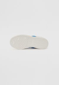 Sole of a white sneaker with circular and triangular tread patterns and a visible blue stripe on the side.