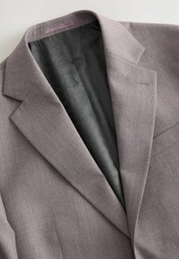Grauer Anzugjacke mit strukturiertem Außenmaterial und glattem schwarzen Innenfutter, das ein geometrisches Muster aufweist. Auffällige scharfe Revers und eine einzelne Tasche.