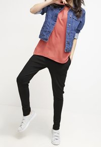 En denimjakke med opfoldede ærmer, en koralfarvet bluse og sorte tapered bukser. Bæres med hvide sneakers med en struktureret sål.
