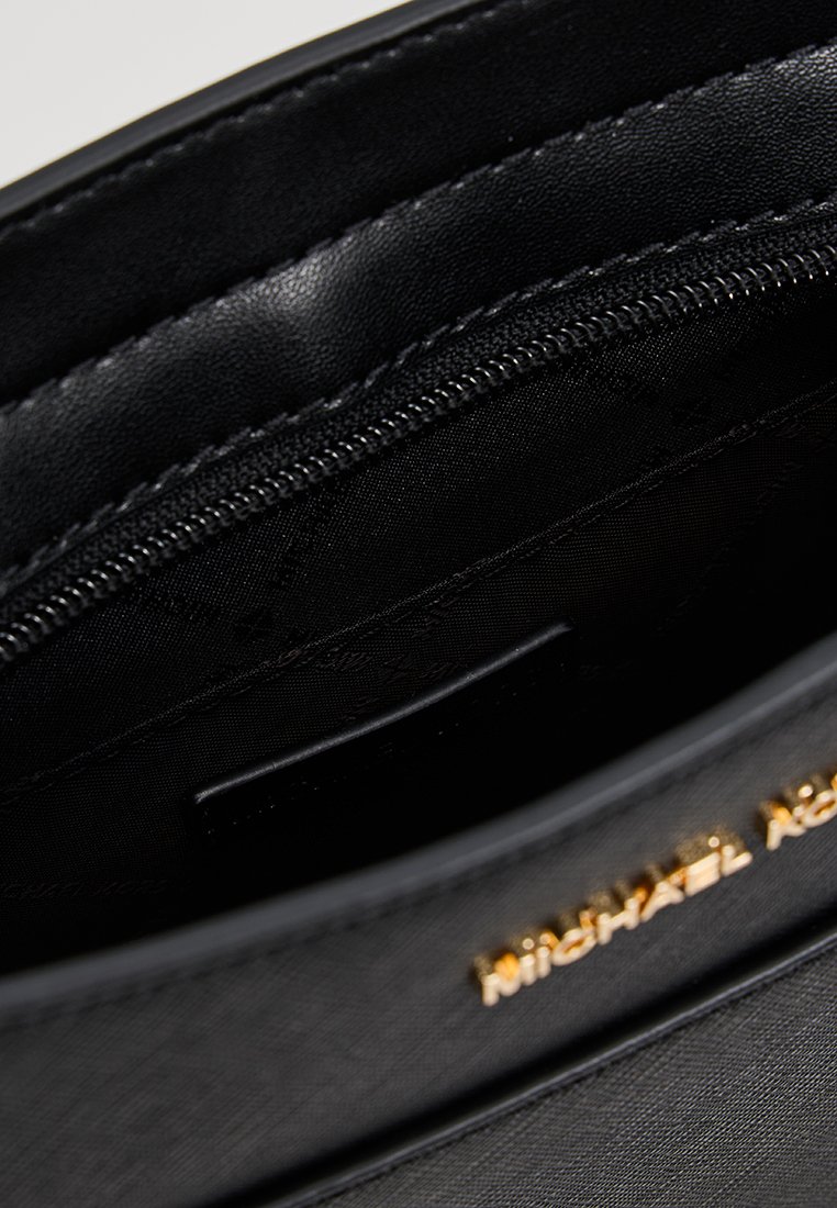 Nahaufnahme des Innenraums einer schwarzen Lederhandtasche, die die Reißverschlusstasche und das goldene Michael Kors-Logo auf der strukturierten Außenseite zeigt.