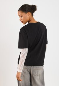 Svart bomull t-skjorte med korte ermer, kombinert med en hvit blond skjorte med lange ermer under. Løse grå denimjeans.