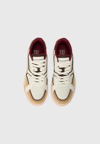 Witte en beige sneakers met geperforeerde textuur, zwarte accenten en bordeauxrood voering. Beschikt over platte veters en een merkreliëflabel op de tong.