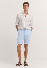 Light blue linen shorts with an elastic waistband and drawstring, paired with a white long-sleeve linen shirt and dark sandals.
