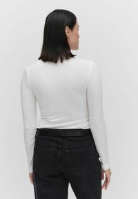 Witte top met lange mouwen gemaakt van rekbaar materiaal, gecombineerd met hoge zwarte jeans, met een gladde textuur en een klassiek ontwerp.
