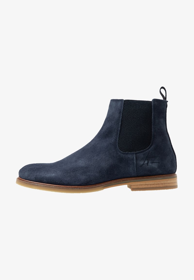 Botte Chelsea en daim bleu marine avec panneau latéral en élastique noir, semelle en bois marron et languette à l'arrière.