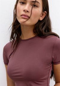 Top scurt de culoare burgundy, din material neted, având un decolteu rotund și cusături pentru un design ajustat.