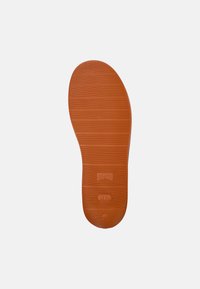 Brown rubber shoe sole with horizontal ridges, rounded toe, and stamped branding. The underside features a circular pattern for traction.
