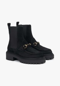 Černé sametové chelsea boty s robustní černou gumovou podrážkou, přední část s třásněmi a zlatým kováním a elastickými bočními panely pro snadné obutí.