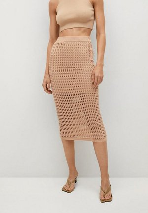 Femme portant une jupe midi beige en tricot avec un motif ajouré, un top court assorti et des sandales beiges à talons.