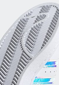 Vit sneakersula med texturerad yta, utrustad med åsar och spår. Sidan har iriserande remsor och små perforeringar.