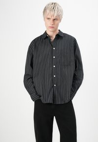 Black and white striped button-up shirt with a chest pocket, featuring a relaxed fit and smooth fabric texture.