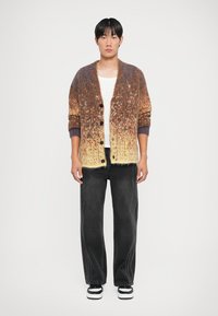 Kootud kardigan, millel on gradient värvid pruunist kreemini, pehme tekstuur, soonilised lillad varrukad ja suured mustad nööbid. Kantud tumesiniste juhtumitega.