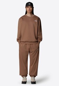 Sudadera marrón y joggers hechos de una tela suave, con un corte holgado, puños acanalados y un pequeño logo en el pecho y el muslo.