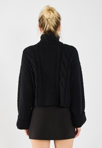 Pull noir court avec motif en maille torsadée, col haut et larges poignets côtelés. Présente un tissu texturé et un tricot épais.