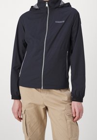 Person wearing black zip-up hooded jacket with side zipper pockets and beige cargo pants with flap pockets.