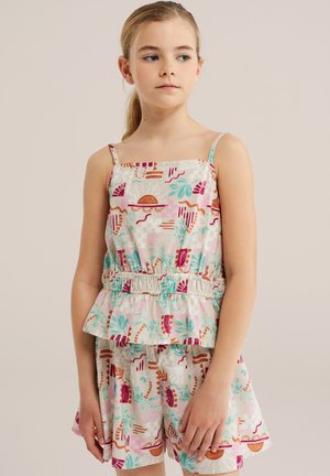 Junges Mädchen mit zurückgebundenem blonden Haar, das ein ärmelloses, gemustertes Oberteil und passende Shorts mit abstrakten floralen Mustern trägt.