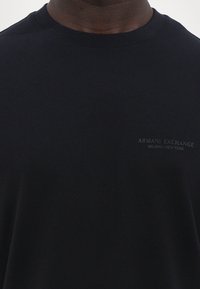 Svart bomulls T-skjorte med rund hals, med en subtil preget logo på venstre side som leser "ARMANI EXCHANGE MILANO/NEW YORK."