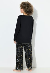 Černý top s dlouhým rukávem a zlatým lemováním, ve spojení s volnými kalhotami s kosmickým potiskem v modré, žluté a bílé na černém pozadí.