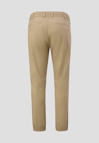 Beige lichte broek met een elastische tailleband, twee achterzakken, taps toelopende pijpen en elastische boorden bij de enkels. Gladde textuur.