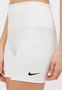 White high-waisted shorts made of stretchy fabric, featuring a black Nike logo on the thigh and flat stitching for added comfort.