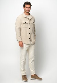 Giacca camicia in misto lana beige con due taschini sul petto e bottoni scuri, abbinata a pantaloni crema e sneakers in suede marroni.