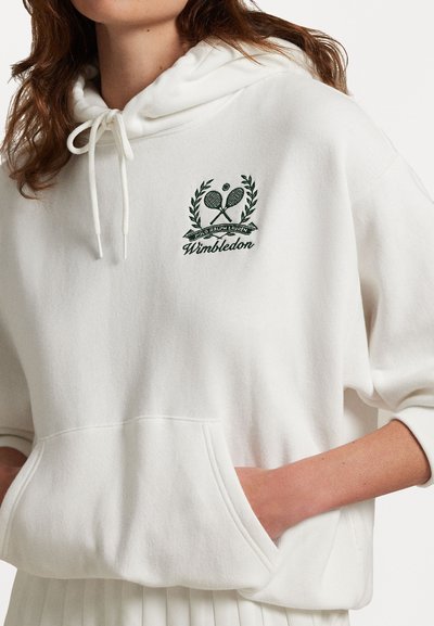 Hoodie blanc avec une capuche à cordon de serrage, ornée d'un logo Wimbledon brodé en vert avec des raquettes de tennis et un laurier, et une poche avant.