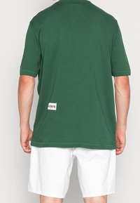 Camiseta de algodón de manga corta en color verde bosque, con corte recto y una etiqueta con "Lacoste" en la parte inferior izquierda.