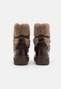 Braune Knöchelstiefel mit einem flauschigen Obermaterial, glatten Lederakzenten und einer strukturierten Sohle. Enthält einen Stoffriemen über die Rückseite.