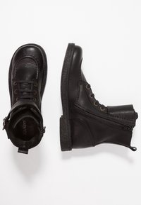 Bottines noires en cuir avec bouts ronds, finition texturée, fermetures à lacets et à zip, et semelles en caoutchouc durable. Caractérisées par des œillets en bronze.